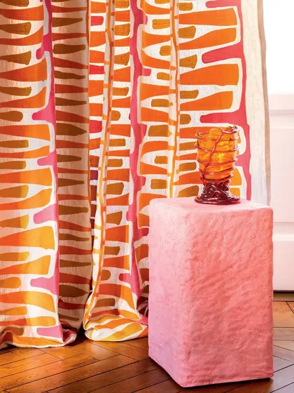 A close-up of the bold, geometric embroidered curtains from Élitis. The vibrant interplay of orange, pink, and brown hues on the fabric showcases how we use statement textiles to inject personality and artistic flair into our drapery designs.