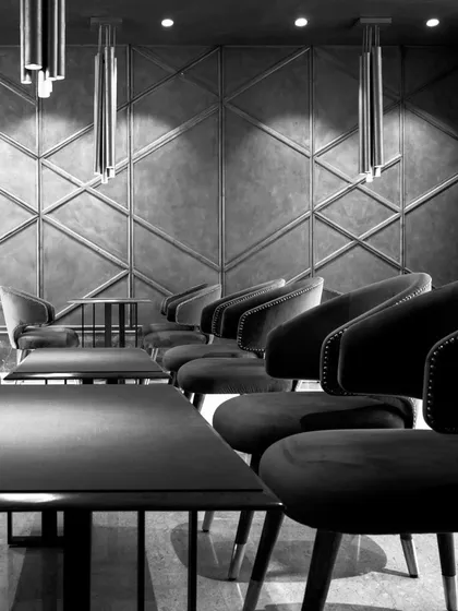 A black and white shot of the main seating area, emphasizing the strong geometric patterns on the wall and the clean lines of the furniture. The lighting is strategically placed to create dramatic highlights and shadows.