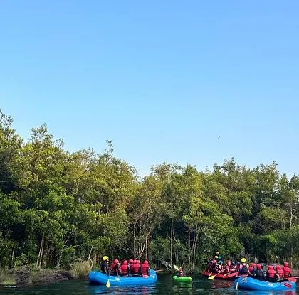 A wide, scenic view of the Kali River in Dandeli, with two rafts full of campers pausing to take in the lush green surroundings.
