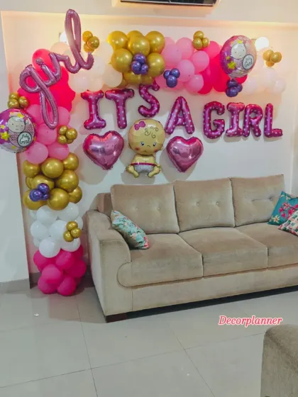 An "It's a Girl" celebration corner. This setup features a vibrant balloon arrangement in pink, gold, and white, with foil letters and baby-themed balloons, perfect for capturing photos of this happy milestone.