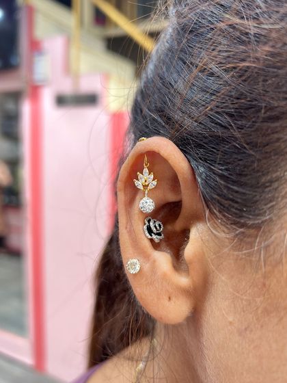A sophisticated stack combining a gold leaf hanging, a black floral conch stud, and a simple diamond stud. This look proves that mixing different styles can create a very chic result.