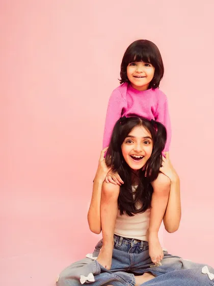 A happy moment between two sisters. The simple pink background makes their joyful expressions pop.