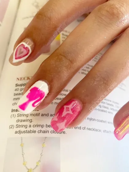 A close-up of this Barbie-themed manicure. It features a hand-painted Barbie silhouette, hearts, and a shimmery pink chrome nail.