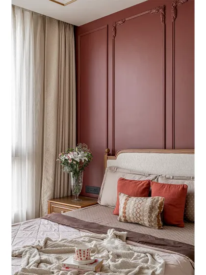 A close-up of the bedside area, showing the custom-built nightstand and the upholstered headboard against a rich burgundy wall. The details, like the molding and the choice of wood finish, are carefully considered to create a serene atmosphere.