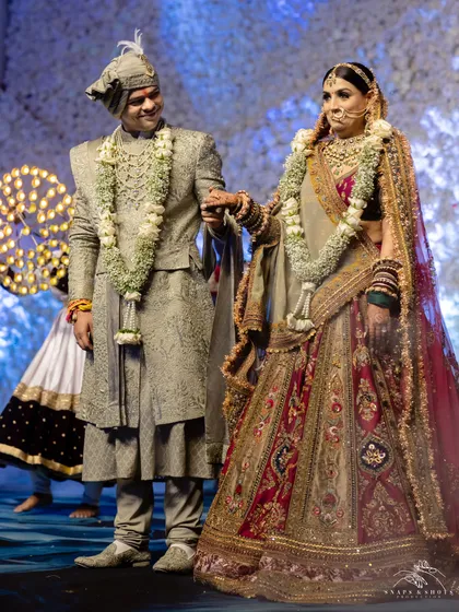 A regal wedding day look. The groom looks dashing in a custom sage green sherwani by Ankit V Kapoor, perfectly complementing the bride's magnificent multi-hued Marwar Couture lehenga.
