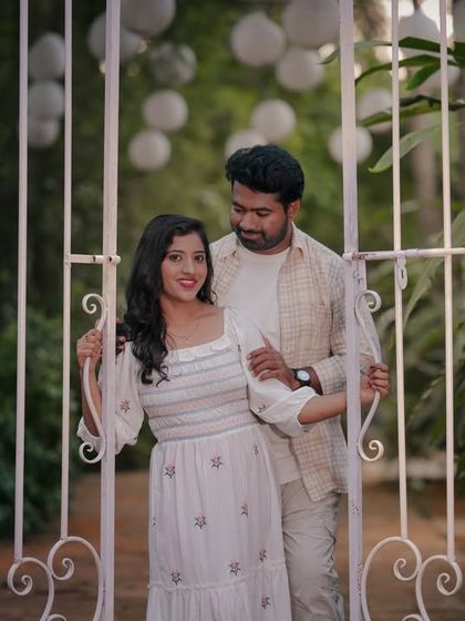 A romantic moment for a couple in matching white outfits, framed by a white garden gate.