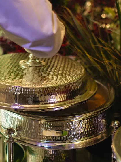 The moment of service, as a white-gloved hand lifts the lid of a chafing dish. This image captures our promise of attentive, high-end service at every event.