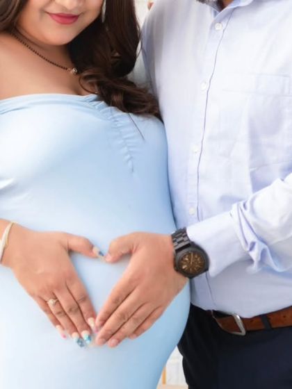 A simple, beautiful gesture. The couple forms a heart with their hands on the baby bump, a universal symbol of their love for the little one on the way.
