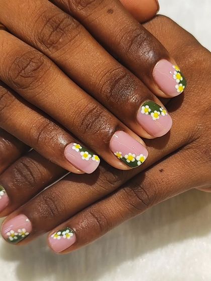 Nails in full bloom. This cute design on short nails features a soft pink base with a half-moon of hand-painted daisies at the cuticle.