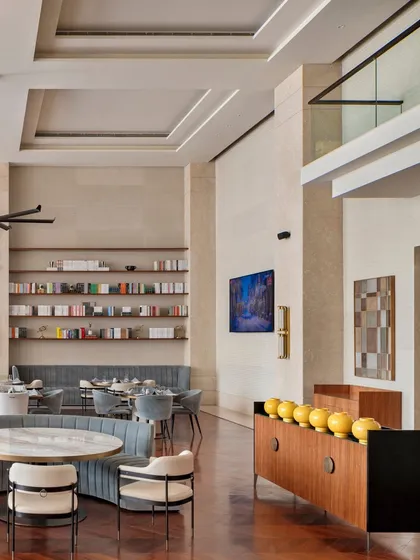 The double-height volume of the clubhouse is balanced with human-scale details. Here, built-in shelving, curated art, and decorative objects add a personal touch to the grand space, making it feel more intimate and lived-in.