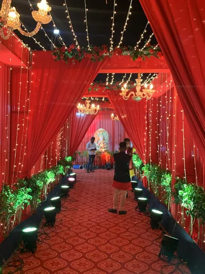 A stunning red entrance walkway for a resort wedding. The path is lined with spotlights and planters, leading through a series of draped archways with chandeliers.