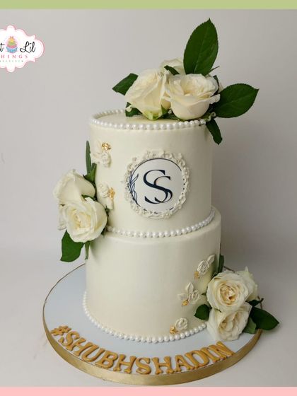 A classic and elegant two-tiered wedding cake. This design features a custom monogram, pearl borders, and is adorned with fresh white roses.