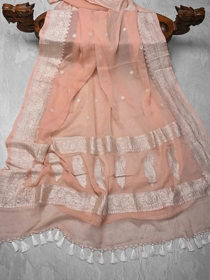 A soft peach chiffon saree with delicate silver butis and a woven silver border. The tassels on the pallu add a playful touch to this elegant saree.