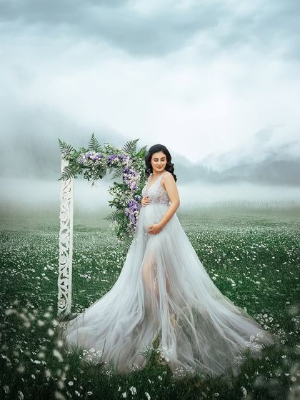 Standing in a field of white flowers with a misty mountain backdrop, this portrait is pure magic. The flowing gown and floral arch complete this fairytale pregnancy scene.