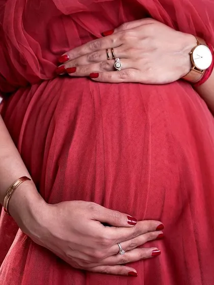 A close-up shot focusing on the baby bump, with the mother's hands gently cradling her belly. This image, highlighting the vibrant red dress, captures the anticipation and love of pregnancy.