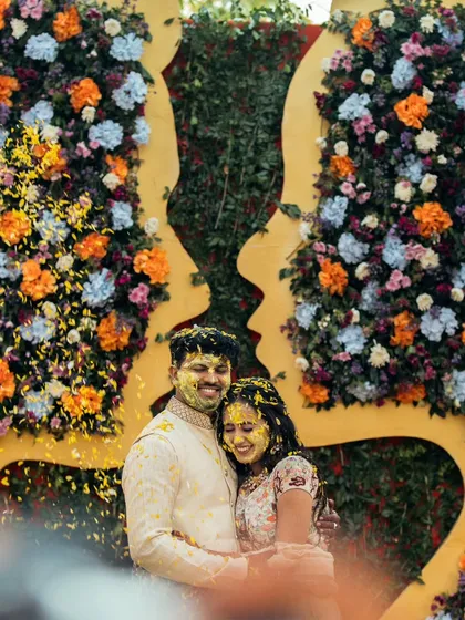 The pure, unadulterated joy of a Haldi ceremony. Anisha and Rishabh are showered with flower petals against a stunning floral backdrop, a candid moment that perfectly captures the vibrant energy and love surrounding them.
