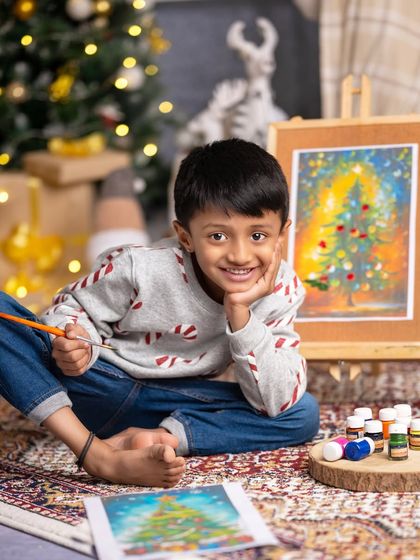 A young artist proudly shows off his Christmas painting, his smile as bright as the colors on his canvas.