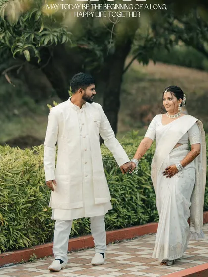A couple dressed in elegant all-white traditional attire walks hand-in-hand through a green park. This shot is serene, classic, and full of grace.