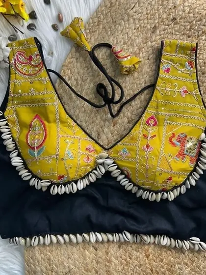 A unique blouse design in yellow and black, featuring traditional motifs and a cowrie shell border. The deep neckline and detailed embroidery make it a standout piece.