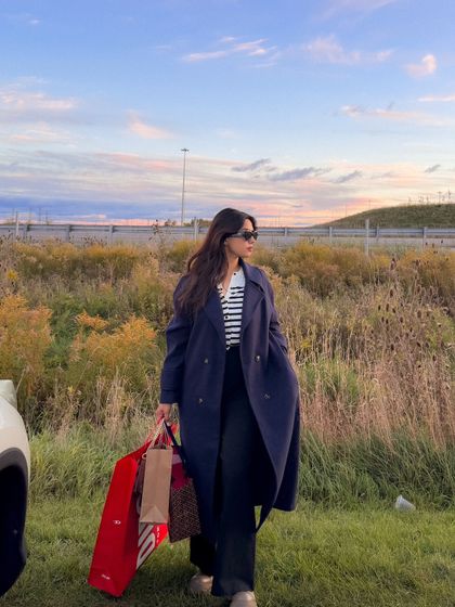 A walking shot, showing the movement of the trench coat and the shopping bags.