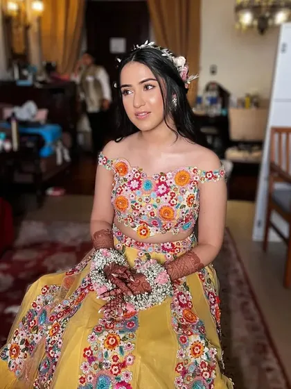A seated bride with her hair in a lovely boho-chic style with a floral crown. This relaxed hairstyle is perfect for a fun and festive Mehendi party.