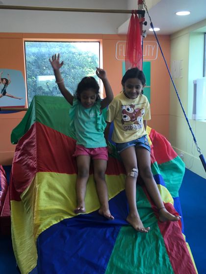 Two friends enjoying a moment on top of the colorful parachute. Our activities encourage social interaction and cooperation.
