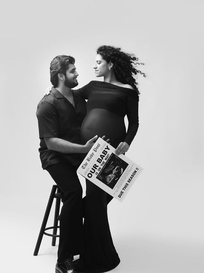Announcing their next chapter in style. This black and white photo combines a loving pose with a creative newspaper prop for a unique and memorable pregnancy announcement.