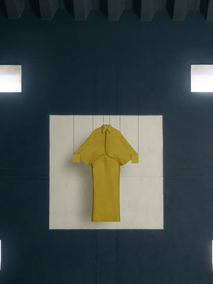 A still-life shot of a yellow dress mounted on the wall. This highlights the garment as a piece of design, framed by the architectural lights of the set.