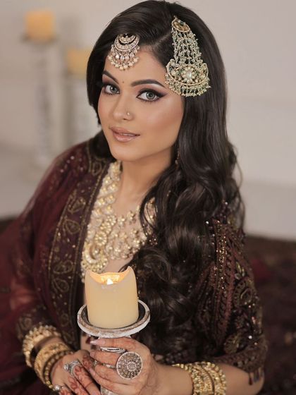 Adorned in timeless elegance, this bride holds a candle, illuminating her beautiful gold-toned jewellery, including a statement necklace, passa, and maang tikka.