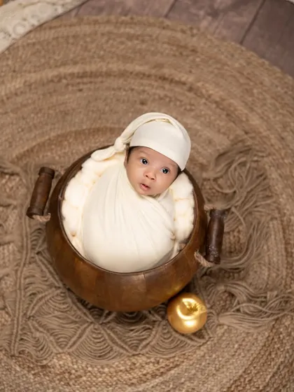 An alert newborn in a wooden bowl, looking right at the camera. The single golden apple prop adds a touch of whimsy to this simple and engaging portrait.