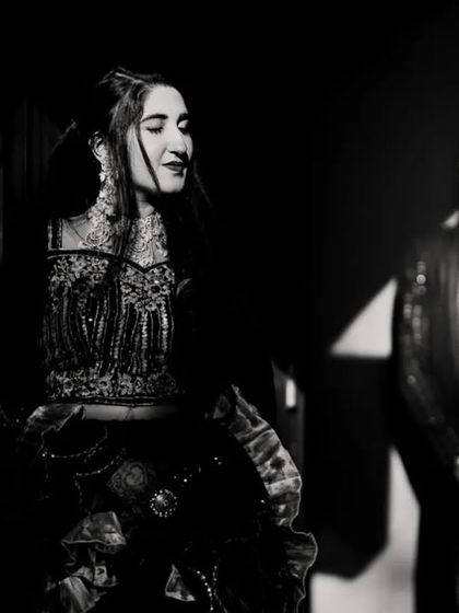 An artistic black and white portrait using shadows and light. The focus is on the bride, creating a moody and dramatic pre-wedding event photo.