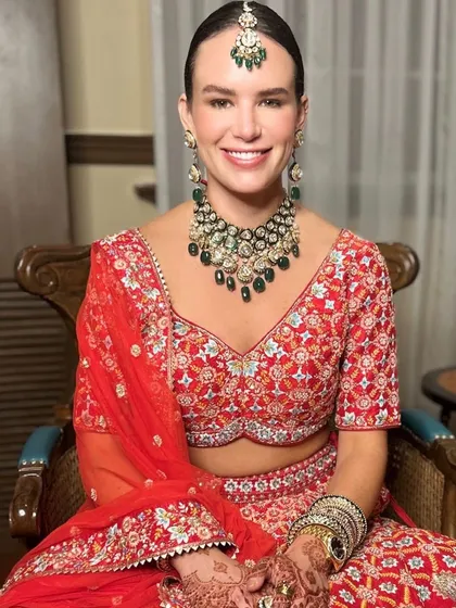 A beautiful smiling bride in her traditional red wedding lehenga. We focused on creating a luminous, long-lasting makeup base and defined eyes, paired with a classic bridal bun and maang tikka, for a truly timeless wedding ceremony look.