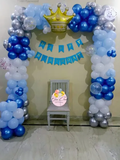 A royal prince theme birthday decoration with a blue, white, and silver balloon arch, topped with a gold crown foil balloon.