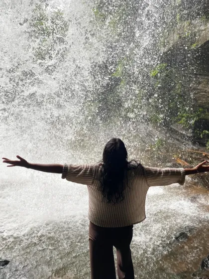 A trekker stands with arms outstretched, embracing the spray of a waterfall on a private Nethravathi trip. A moment of pure freedom.