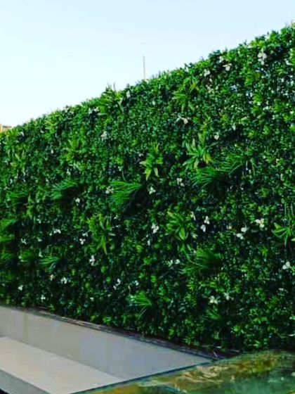 A simple and clean artificial green wall for a balcony or terrace. This design uses a mix of green foliage with small white flowers for a subtle, fresh appearance.
