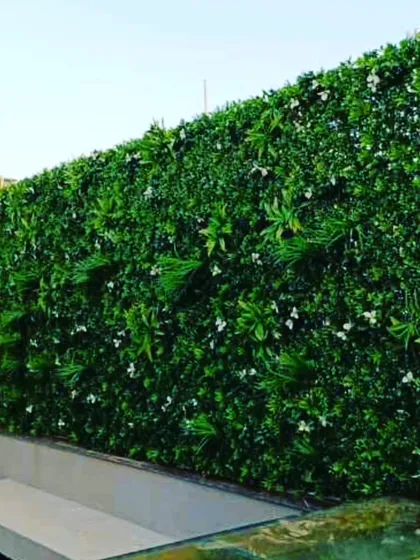 A simple and clean artificial green wall for a balcony or terrace. This design uses a mix of green foliage with small white flowers for a subtle, fresh appearance.