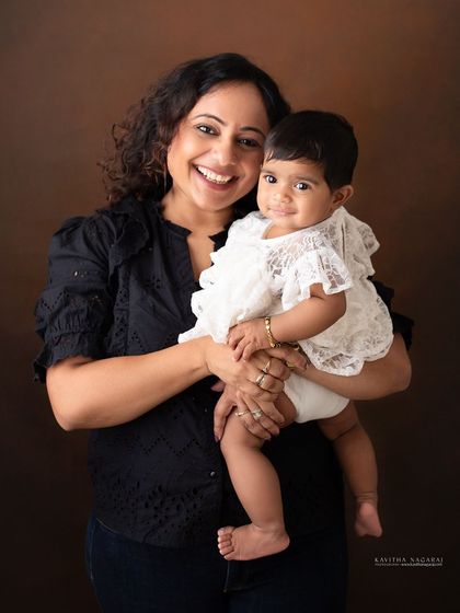 A mother smiles as she holds her eight-month-old daughter. The genuine joy and connection between them is the heart of this beautiful portrait.
