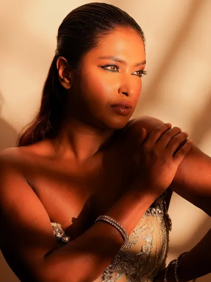 A close-up under dramatic lighting. This highlights the beautiful bronze tones on the skin and the sharp, clean lines of the eye makeup.