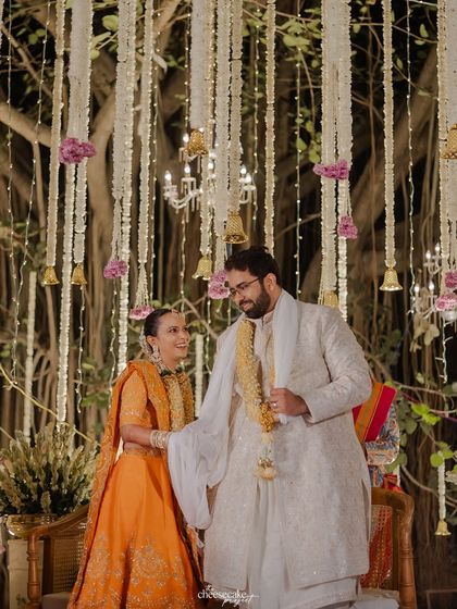 A happy portrait of the couple standing under a beautifully decorated mandap.