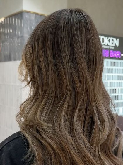 This close-up highlights the cool, ashy tones and the dimension created by the balayage technique, with the Redken gloss bar in the background.