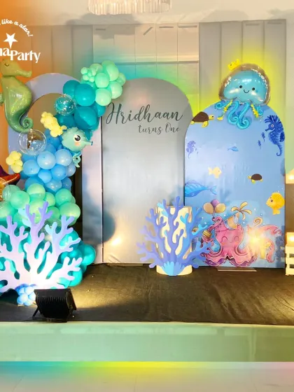 We dove deep to create this magical underwater world for a first birthday party. The setup features a custom backdrop with adorable sea creatures, an organic balloon garland in shades of ocean blue and teal, and charming cutouts of coral, a seahorse, and an octopus. The glowing "1" marquee light adds a special touch to this enchanting aquatic theme.