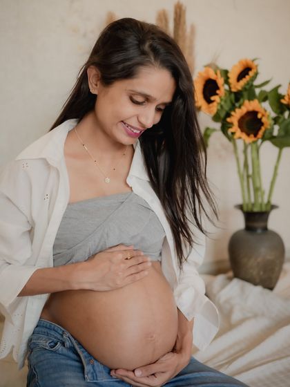 A quiet moment for the mother-to-be, looking down at her baby bump. The sunflowers in the background add a cheerful pop of color to this indoor studio-style shot.
