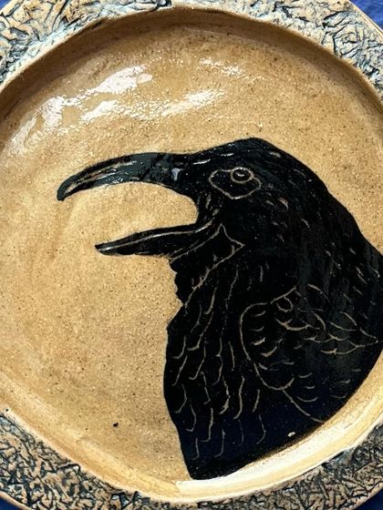 A close-up of the hand-carved crow plate. The sgraffito technique allows for such expressive detail, capturing the texture of the feathers and the bird's sharp eye.