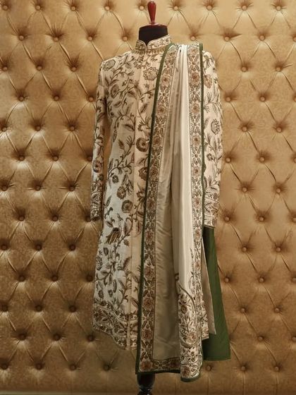 This royal ensemble features an ivory silk sherwani with intricate Resham embroidery, perfectly contrasted with a deep green stole for a touch of color.
