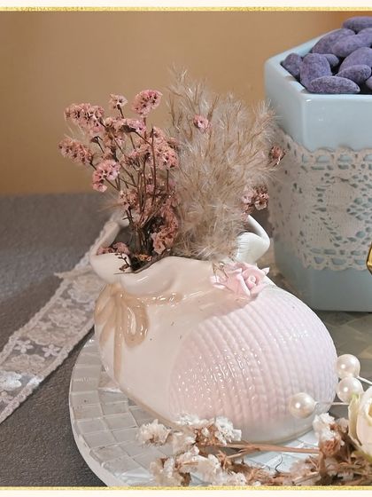 A close-up of the delicate ceramic baby shoe vase, filled with dried baby's breath and pampas grass. It's a sweet keepsake that can be cherished long after the treats are gone.