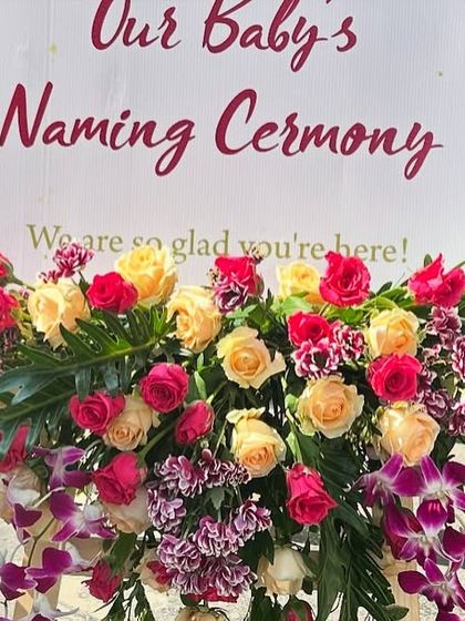 The floral arrangement at the base of the welcome sign, using a mix of roses and orchids to greet guests.