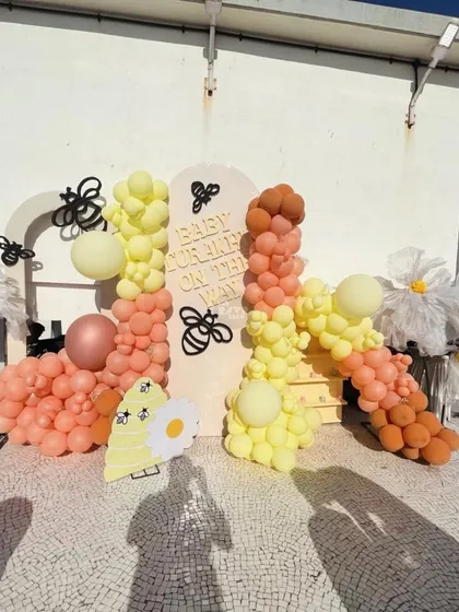 A look at our "Sweet as Can Bee" theme in action on a sunny rooftop. This setup features a vibrant balloon garland in shades of yellow and peach, oversized daisies, and adorable bee accents for a cheerful and playful baby shower celebration.