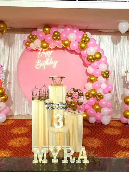 A sweet Peppa Pig theme for Myra's 3rd birthday. This party setup features a pink backdrop, pink, white, and gold balloon arch, and Peppa Pig character cutouts on balloon stands.