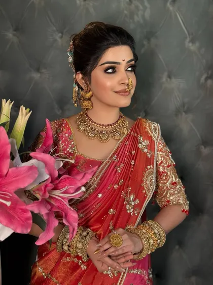 A happy bride in her pink and orange saree, looking away with a smile.