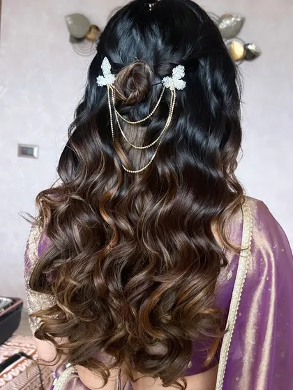 A stunning half-up bun hairstyle, adorned with delicate butterfly accessories and gold chains. This is a perfect example of a modern and romantic bridal hairstyle.
